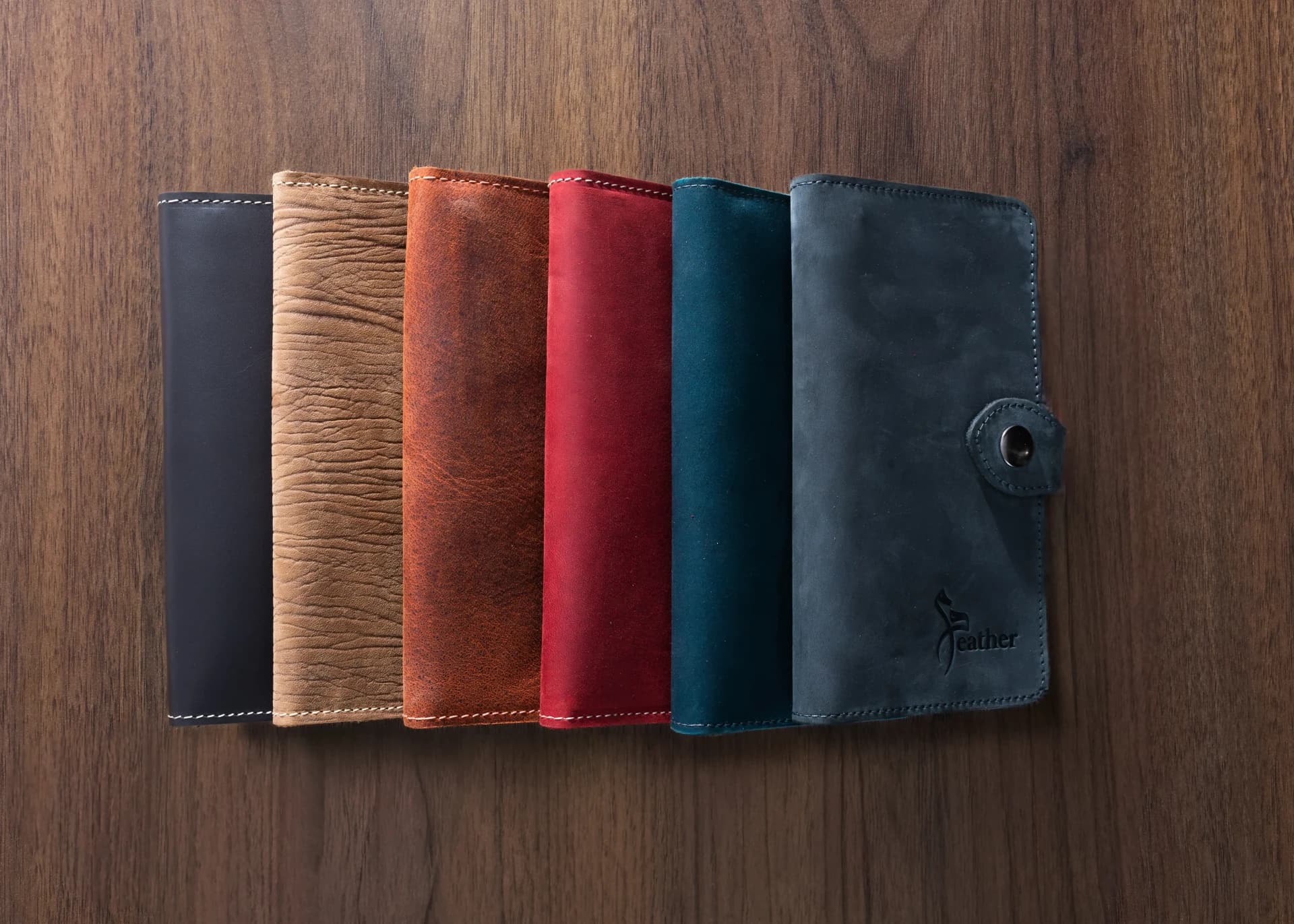 Six XEATHER Nomad travel wallets in assorted leather colours on a wooden surface